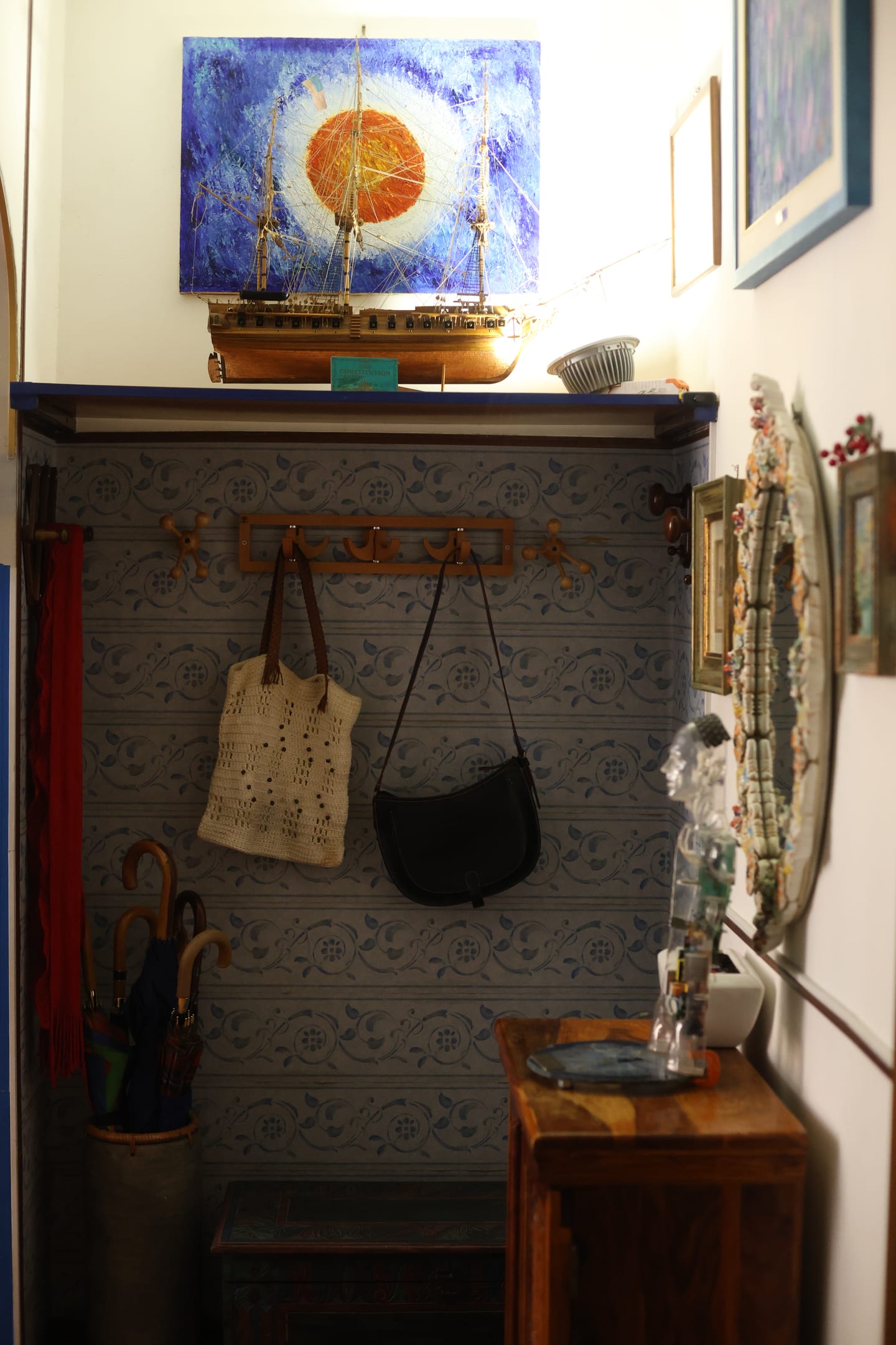 The entrance hall with a coat rack, patterned wallpaper, a model sailing ship on a shelf and a painting of a sun above it