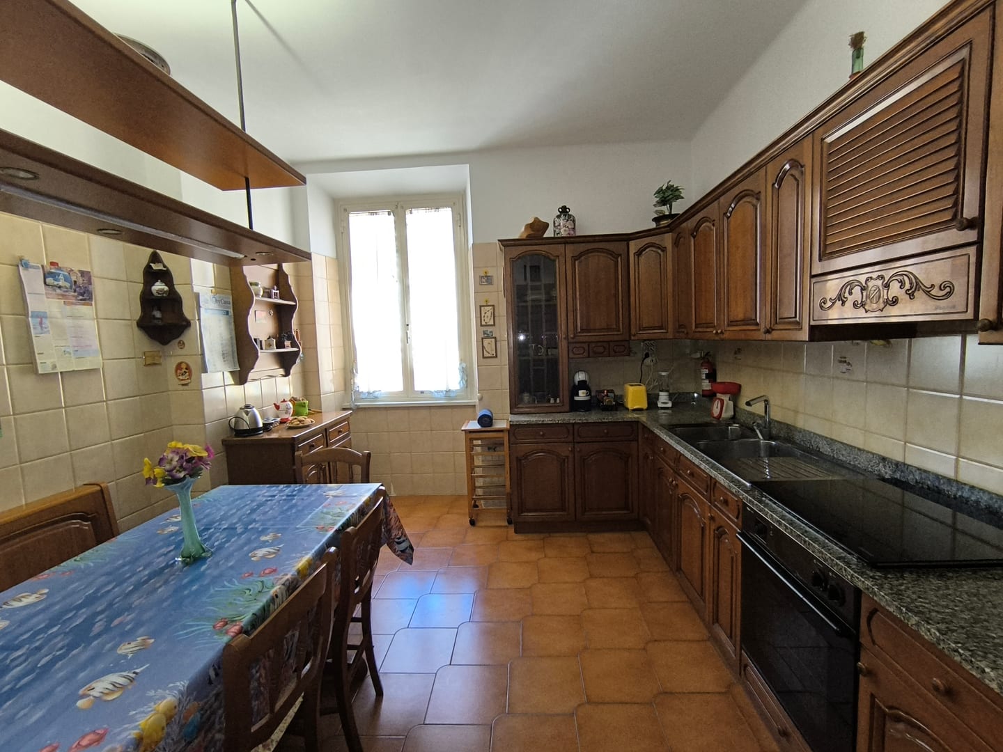 The kitchen seen along its length: wooden cabinets, granite worktops, and a long table with a blue cloth