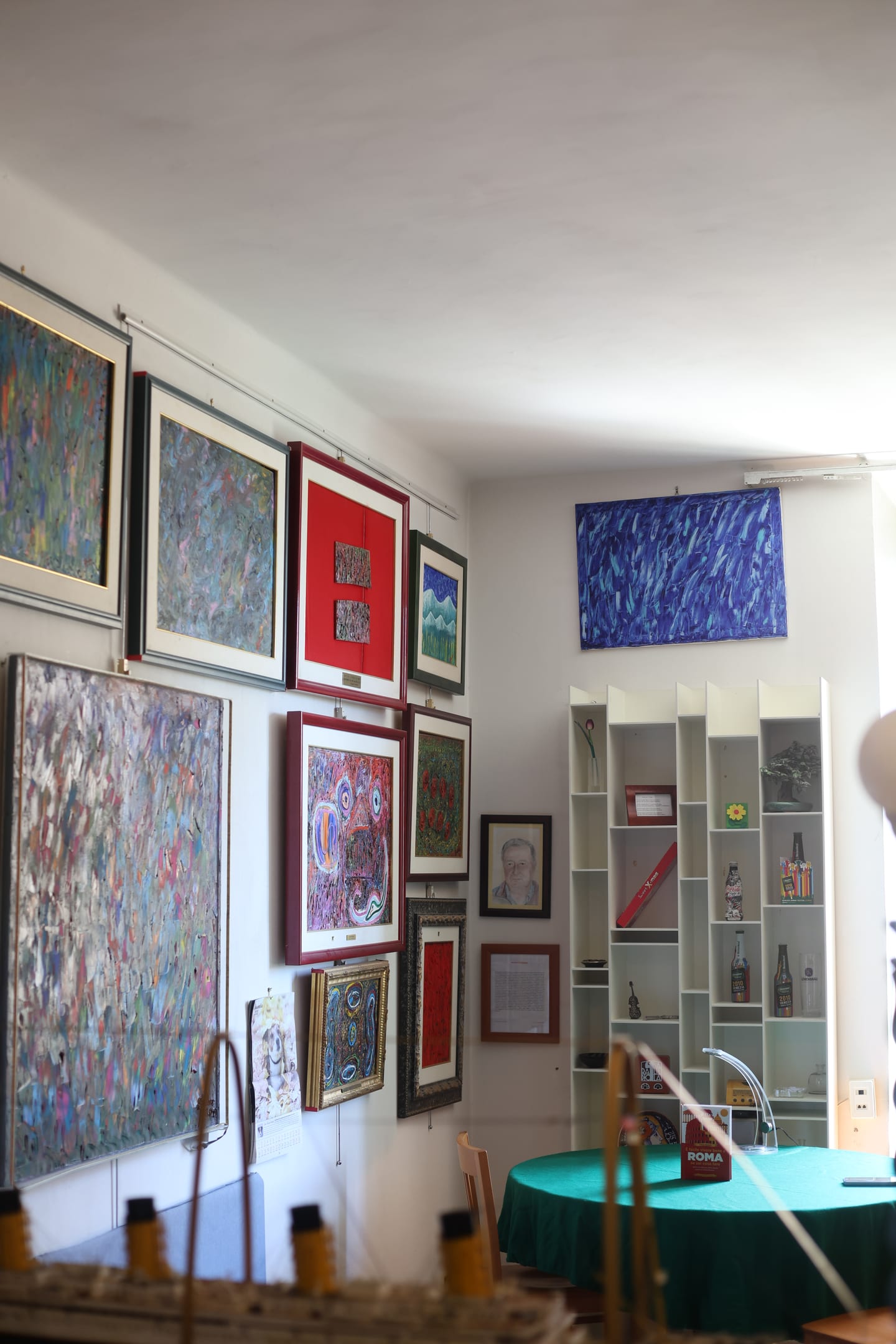 A living room wall densely hung with framed abstract paintings in red, blue and green frames