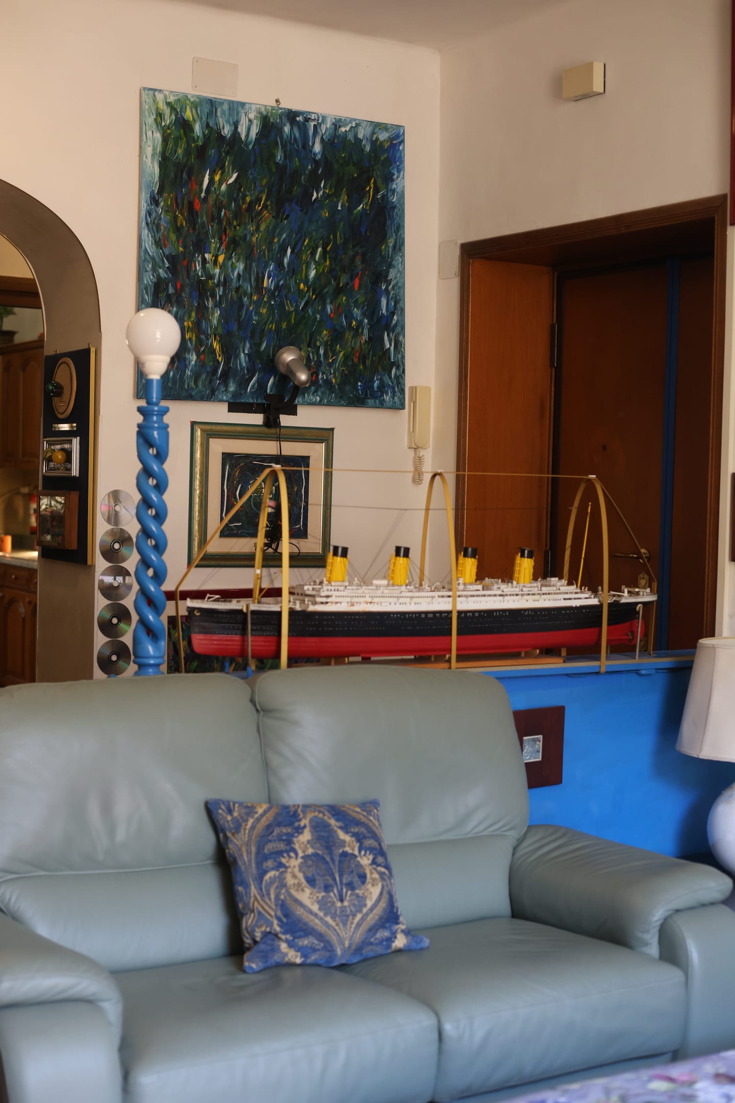 A pale green leather sofa below a large abstract painting, with a model of the Titanic on a blue plinth behind it