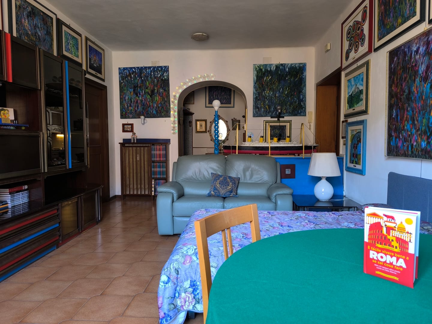 Il salotto con il divano letto aperto, un tavolo coperto di verde e i quadri che riempiono la parete sopra